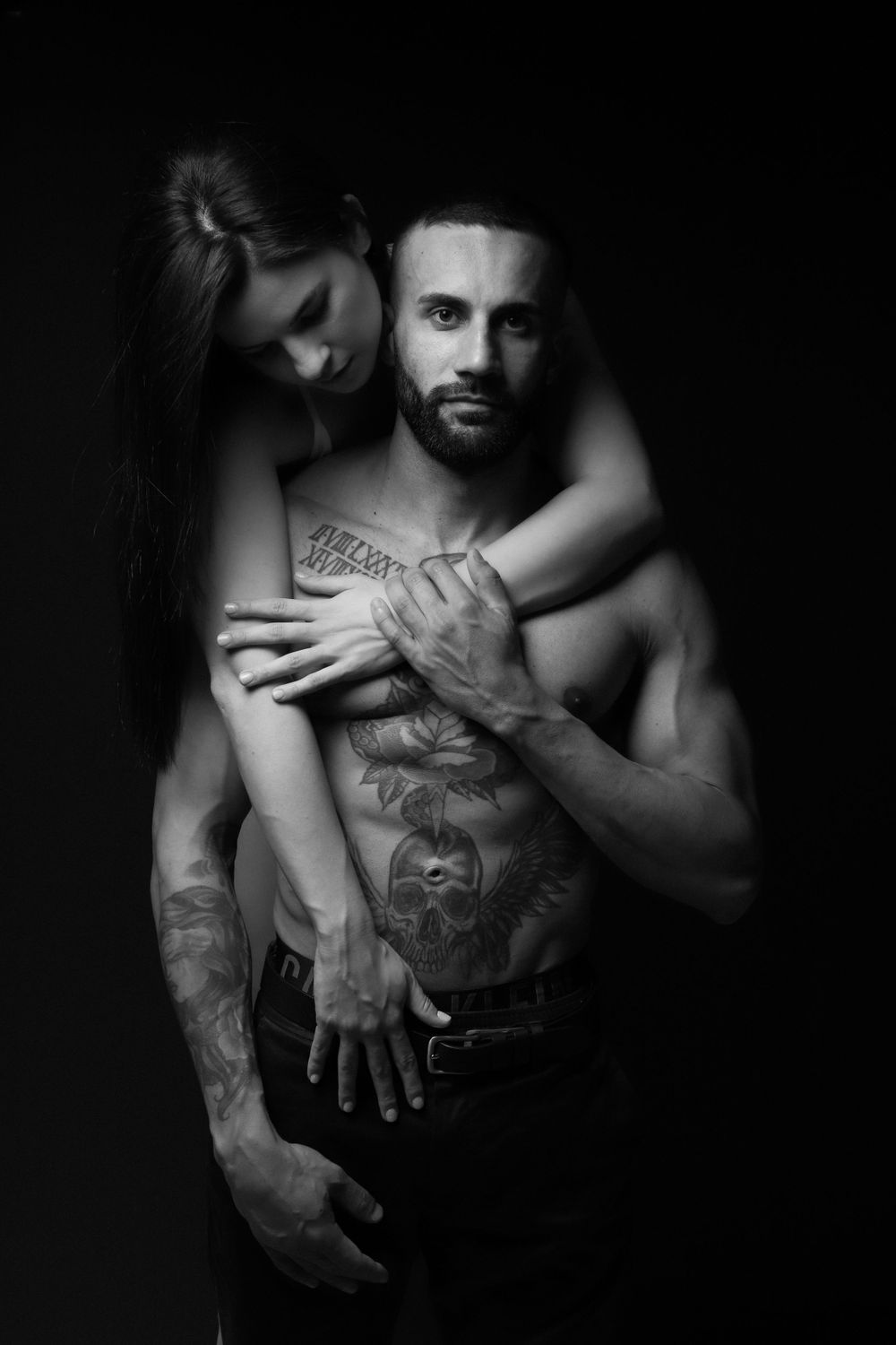 Intimate couple's portrait showcasing tattoo artwork in dramatic lighting.