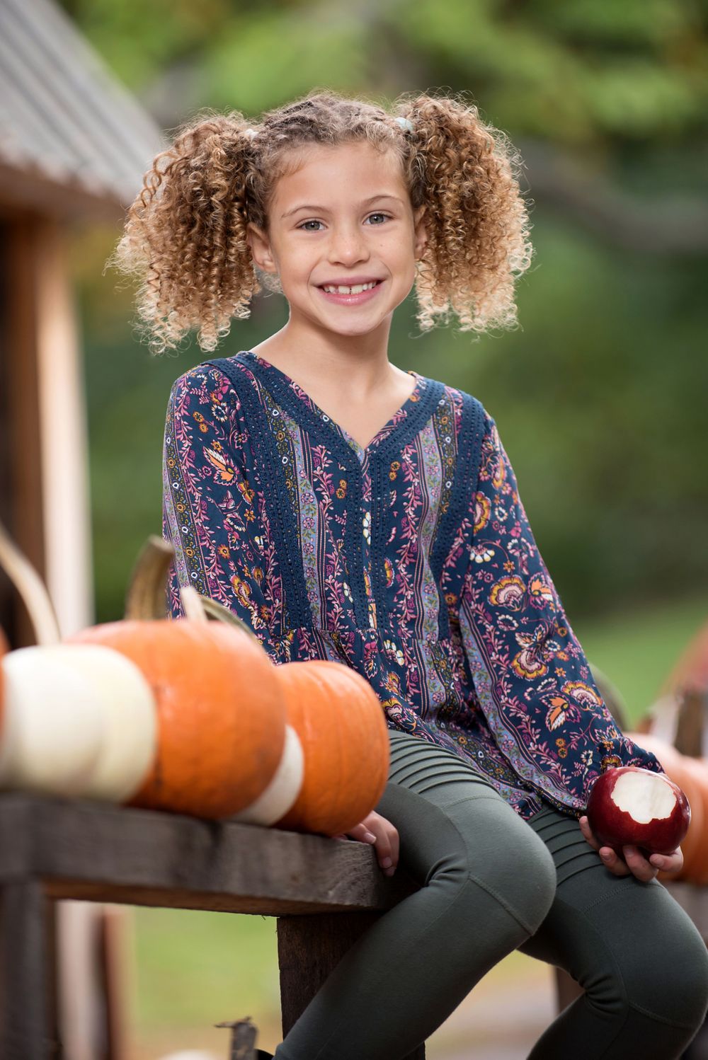 female child model eating an apple amidst pumpkins
