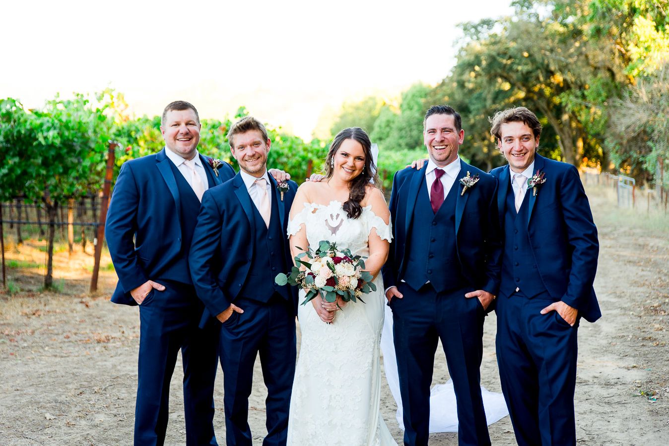groomsmen in navy suits surround bride on dirt path at Pennyroyal Farm