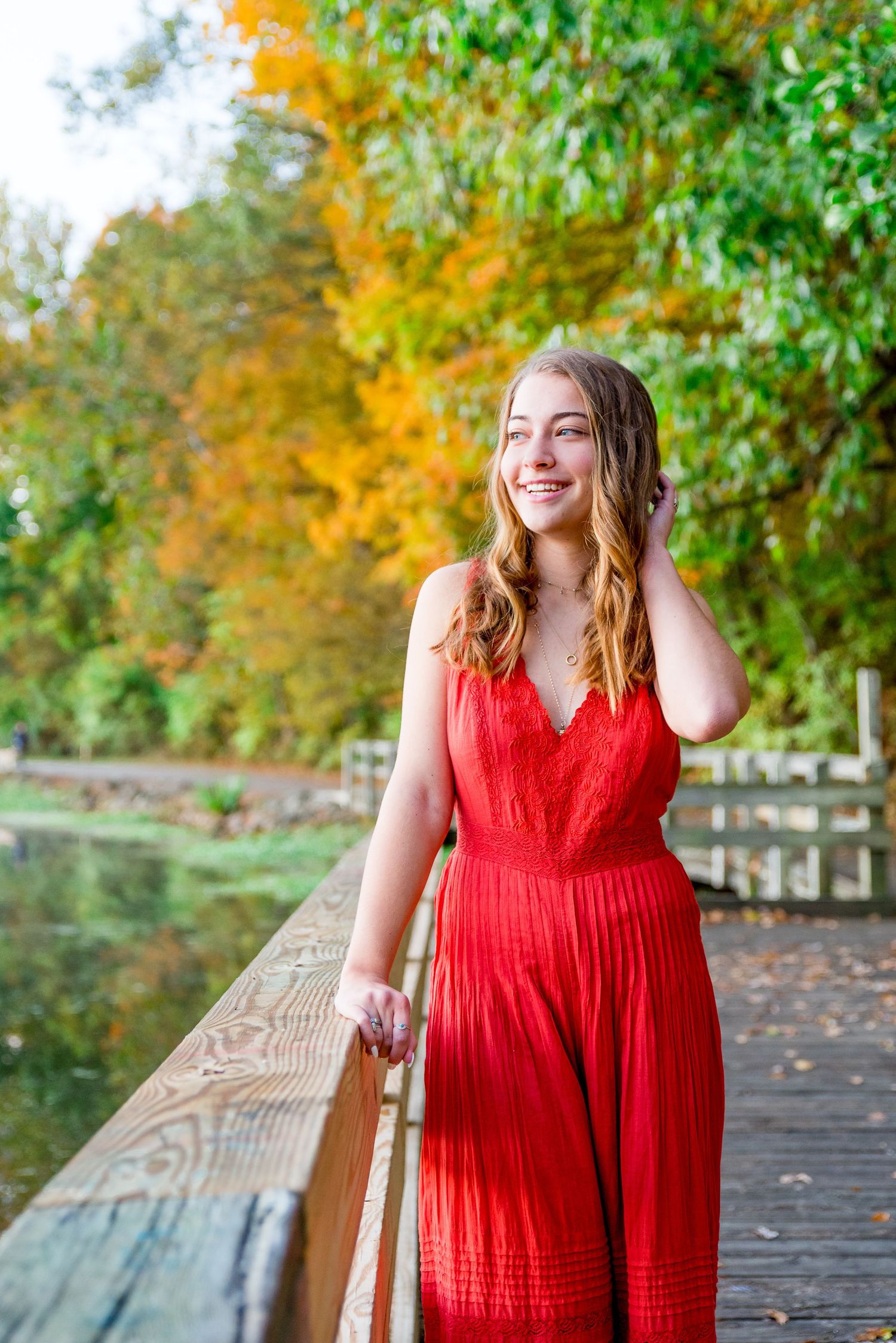 young girl in bright orange jumpsuit standing on a bridge with fall foliage for senior pictures in Chicago
