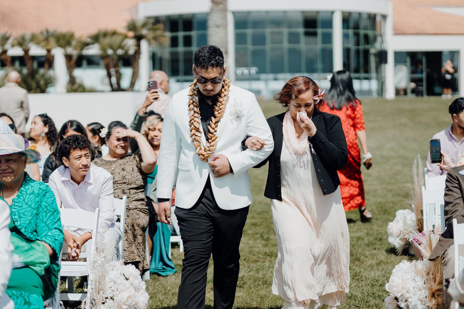 Wedding couple walking down the aisle at an outdoor ceremony by a modern building.