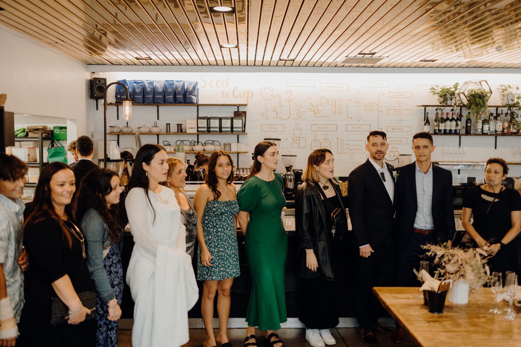 Wedding guests gather in a modern venue with wood-paneled ceiling for a celebration.