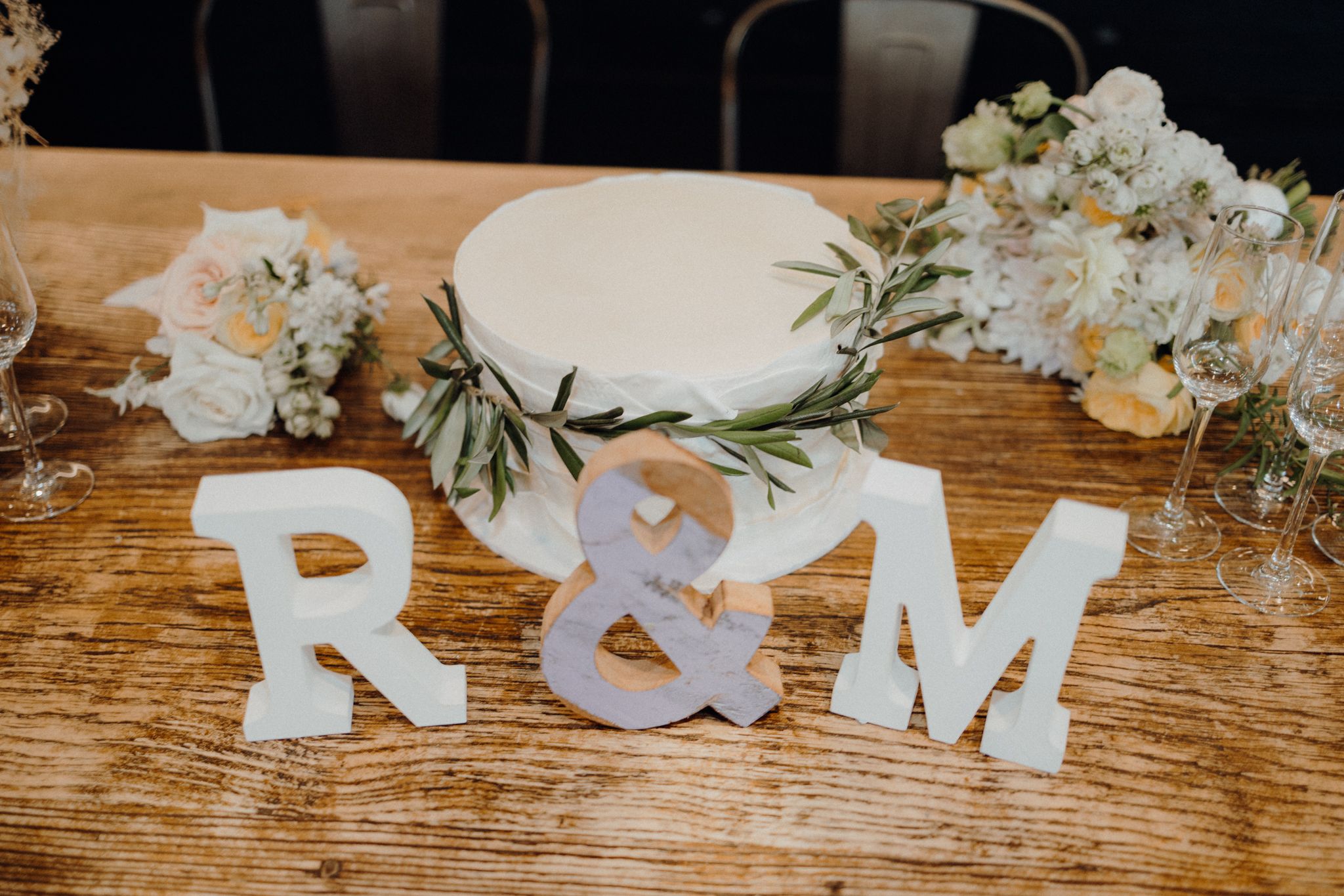 White decorative letters R&M displayed on wooden table with floral arrangements and wedding decor.