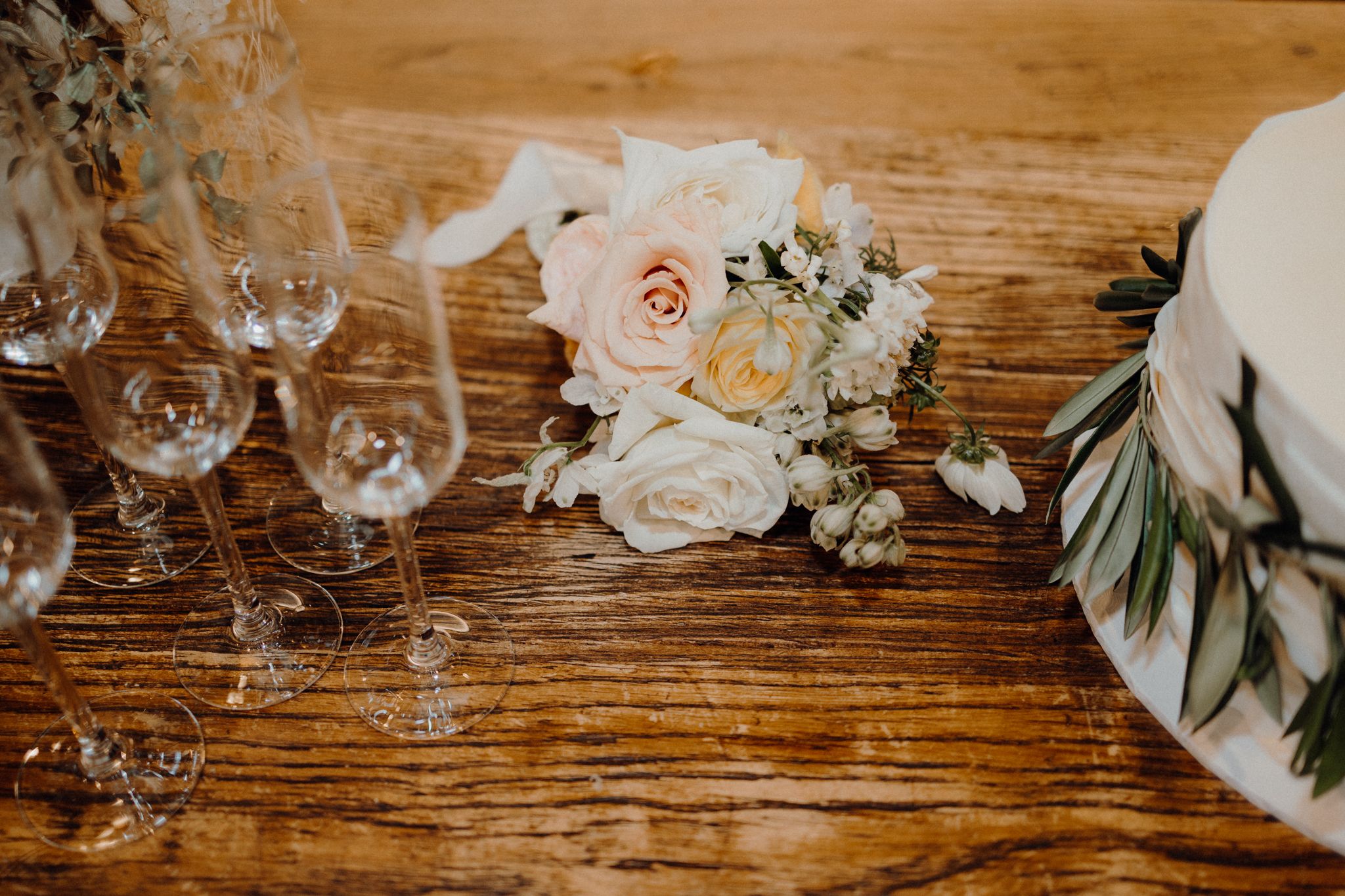 Elegant wedding table setting with pink roses, wine glasses and eucalyptus on rustic wooden surface.