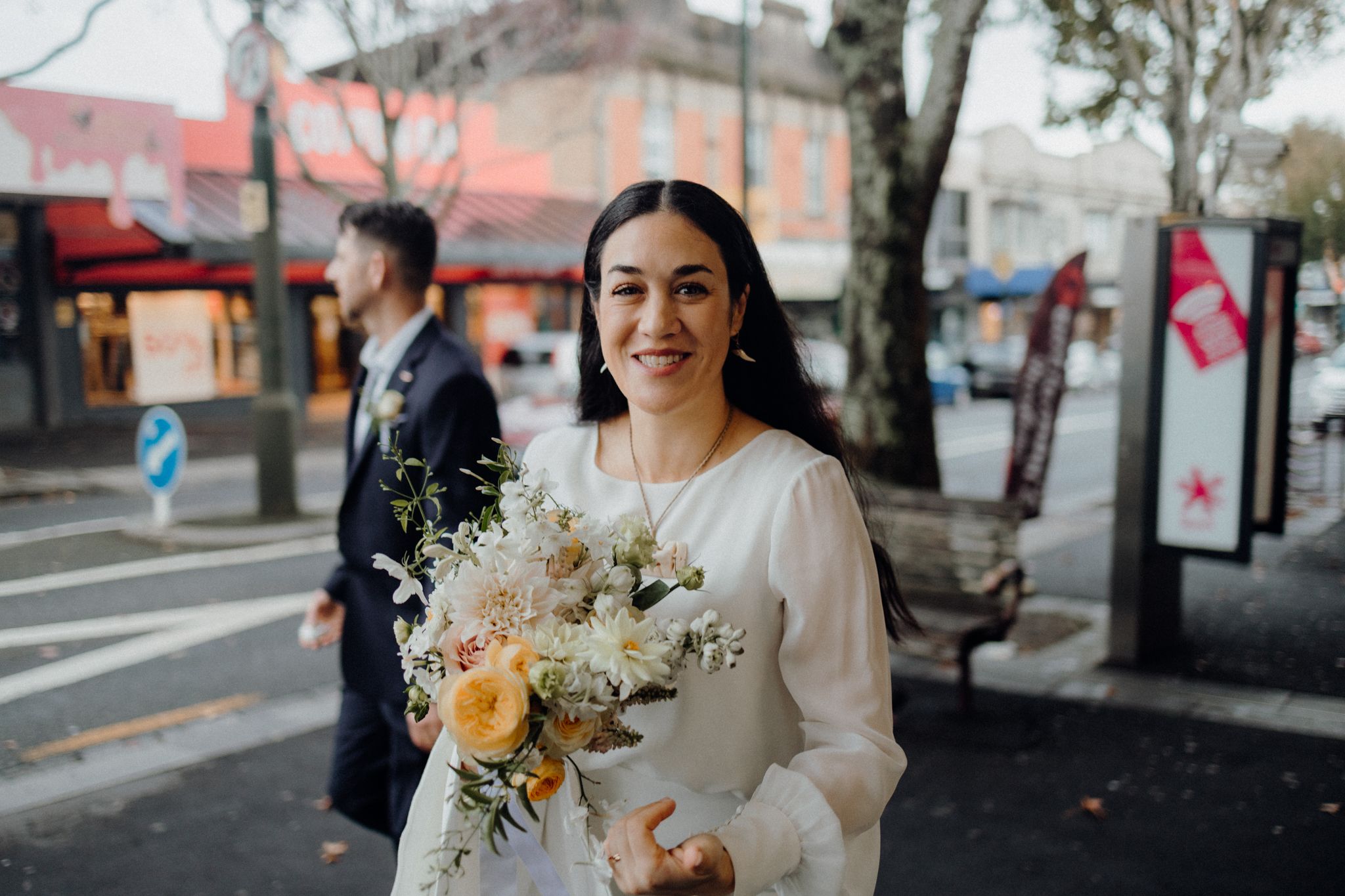 Person in white dress holding a bouquet of flowers on an urban street.