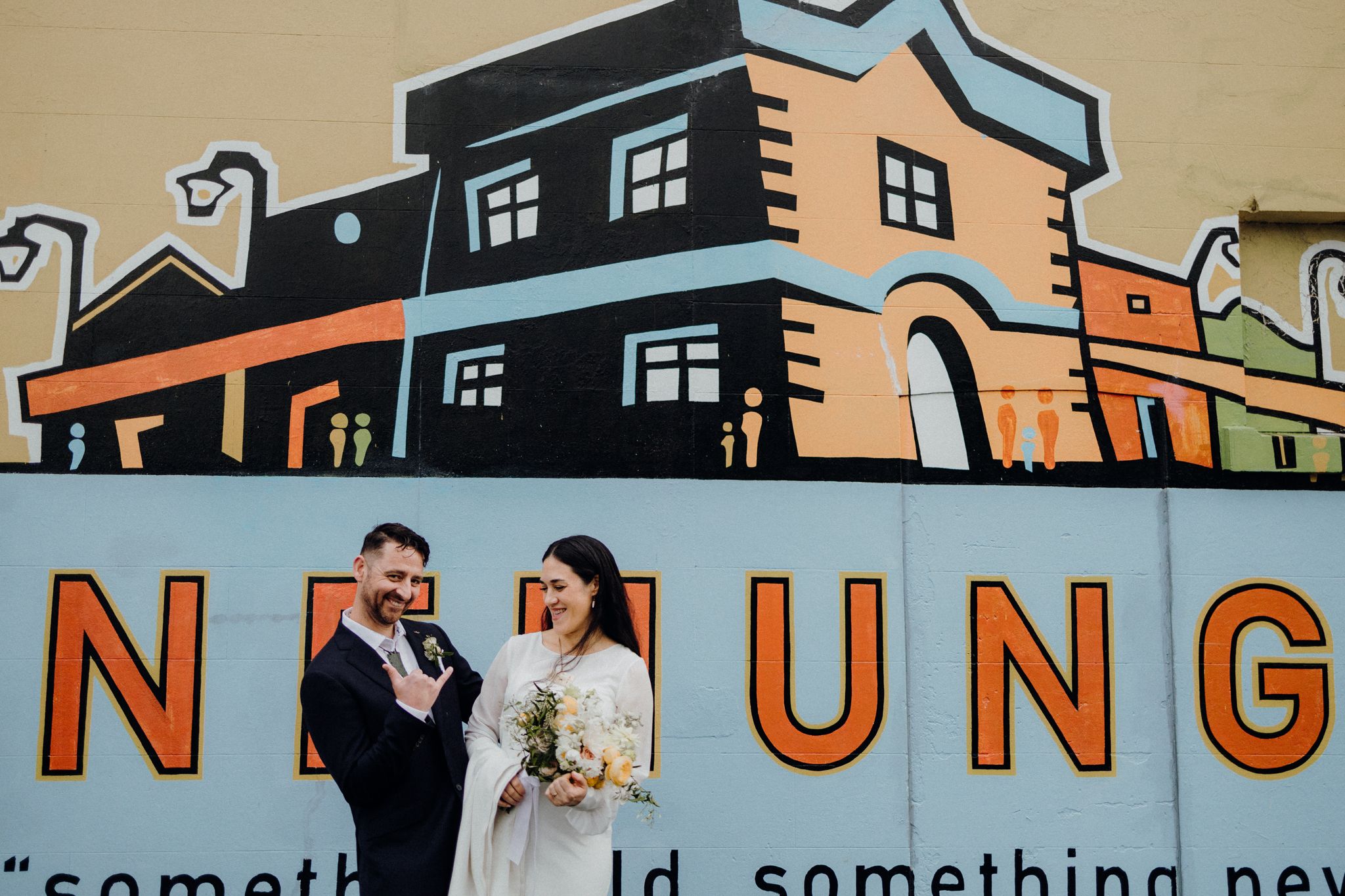 A couple posing in front of a building with large lettering.