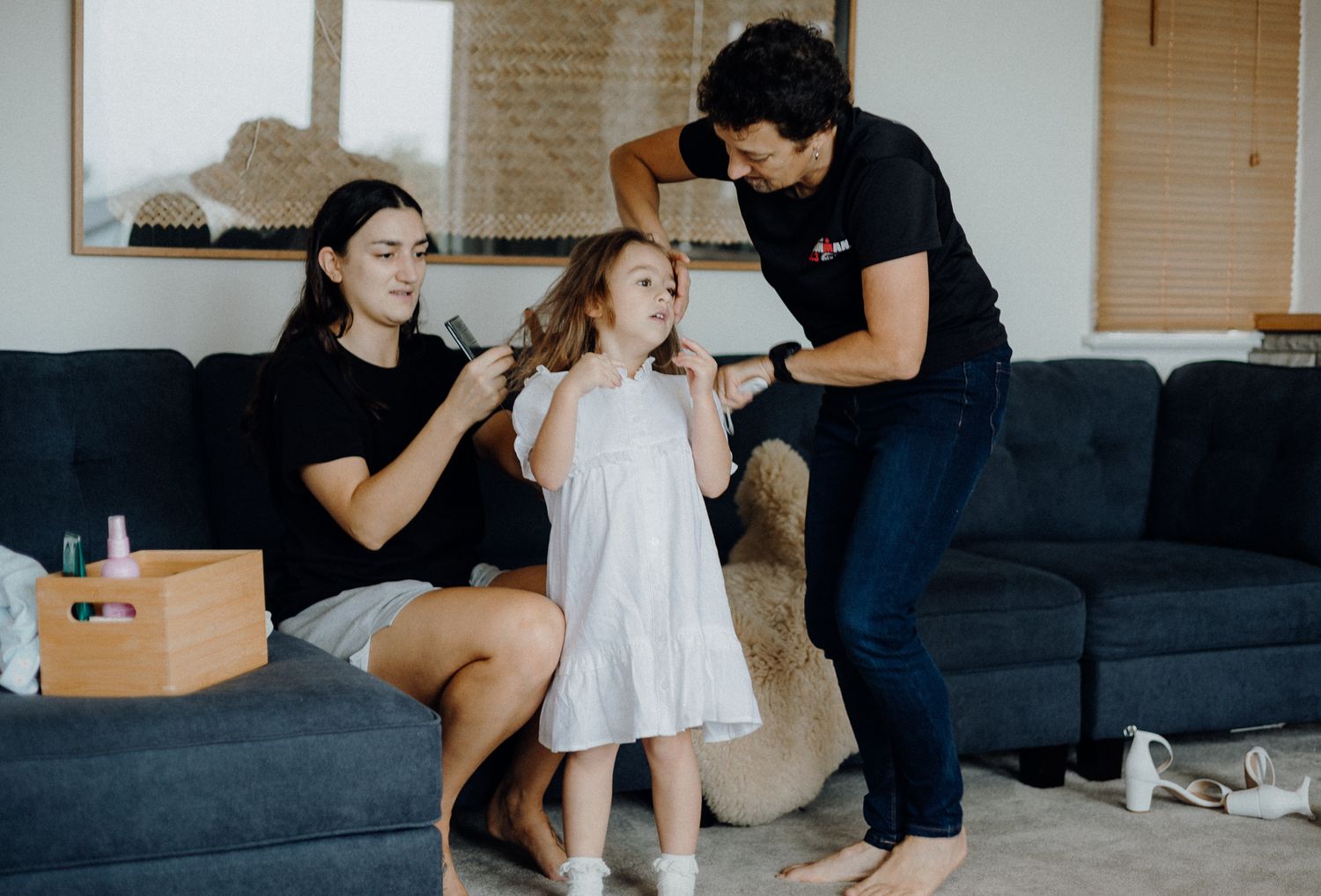 Three people share a joyful moment on a navy blue couch in a living room setting.