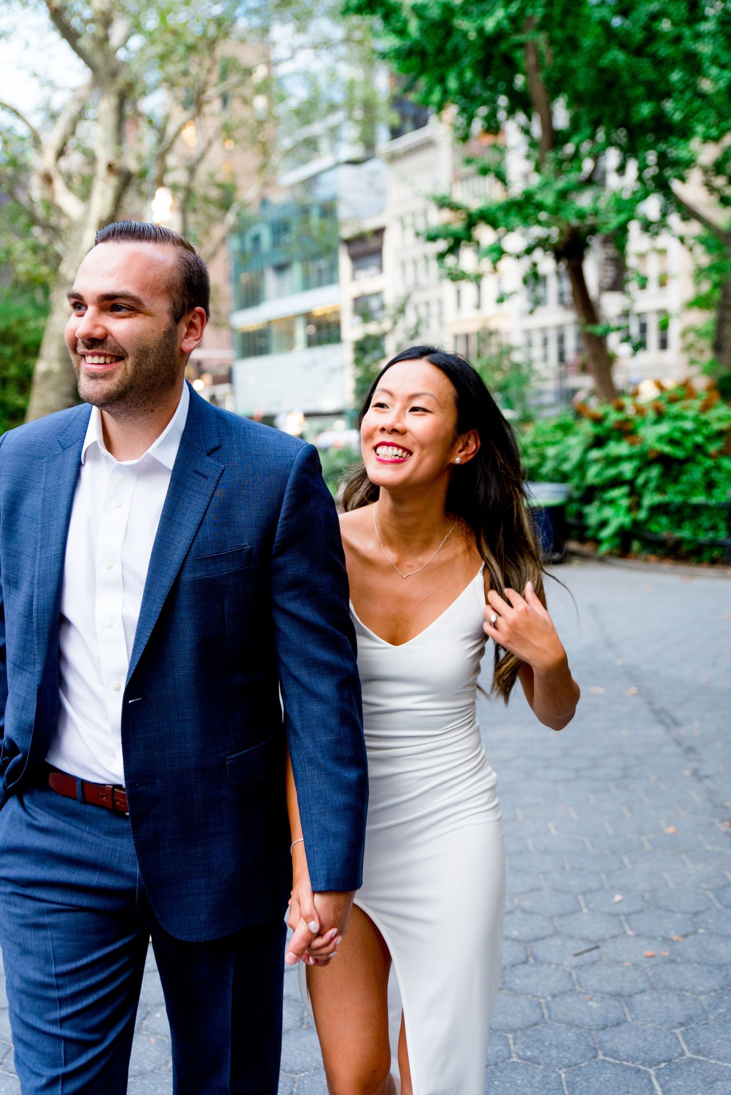 man in navy suit and woman in white dress walking through Flatiron District NYC