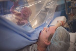 A newborn baby cries as his mother peeks over a c-section blue drape in the operating room immediately after birth