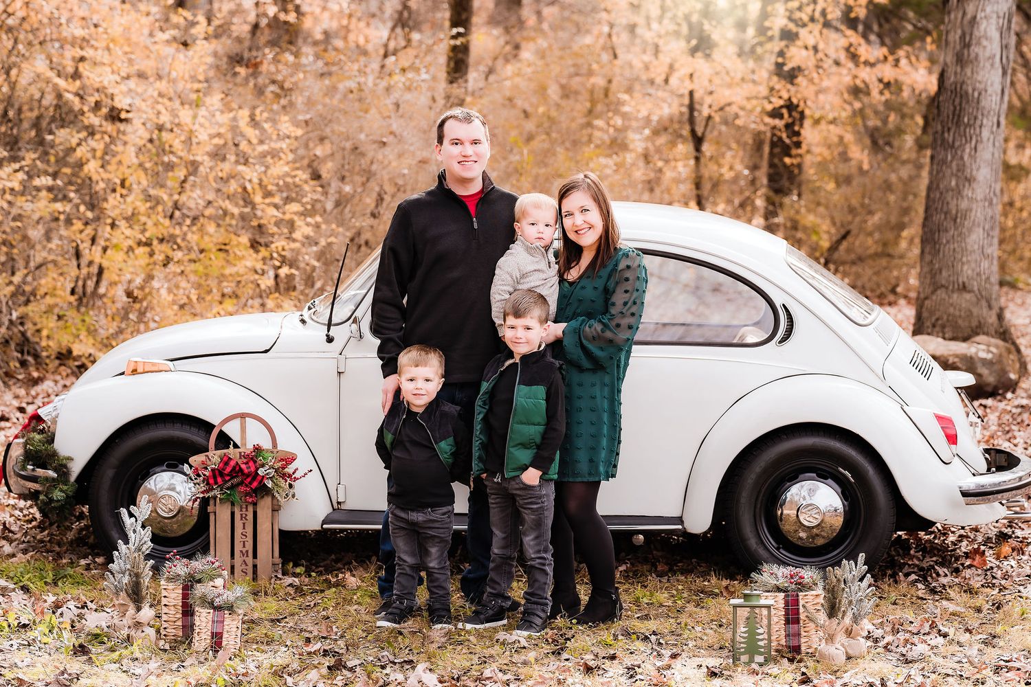 Family poses beside vintage white Volkswagen Beetle during fall season.