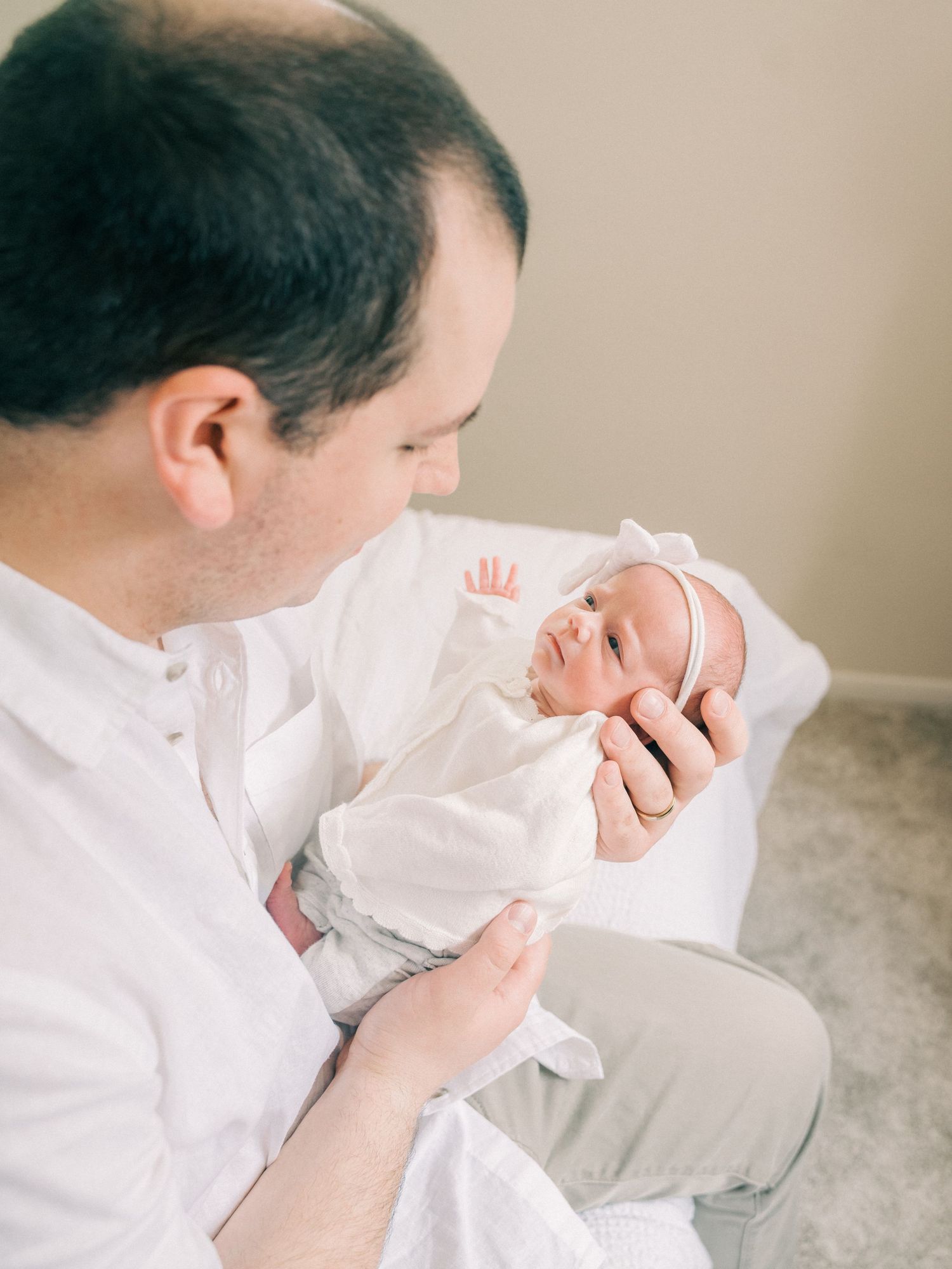 A baby in white clothing being cradled and lovingly gazed at.
