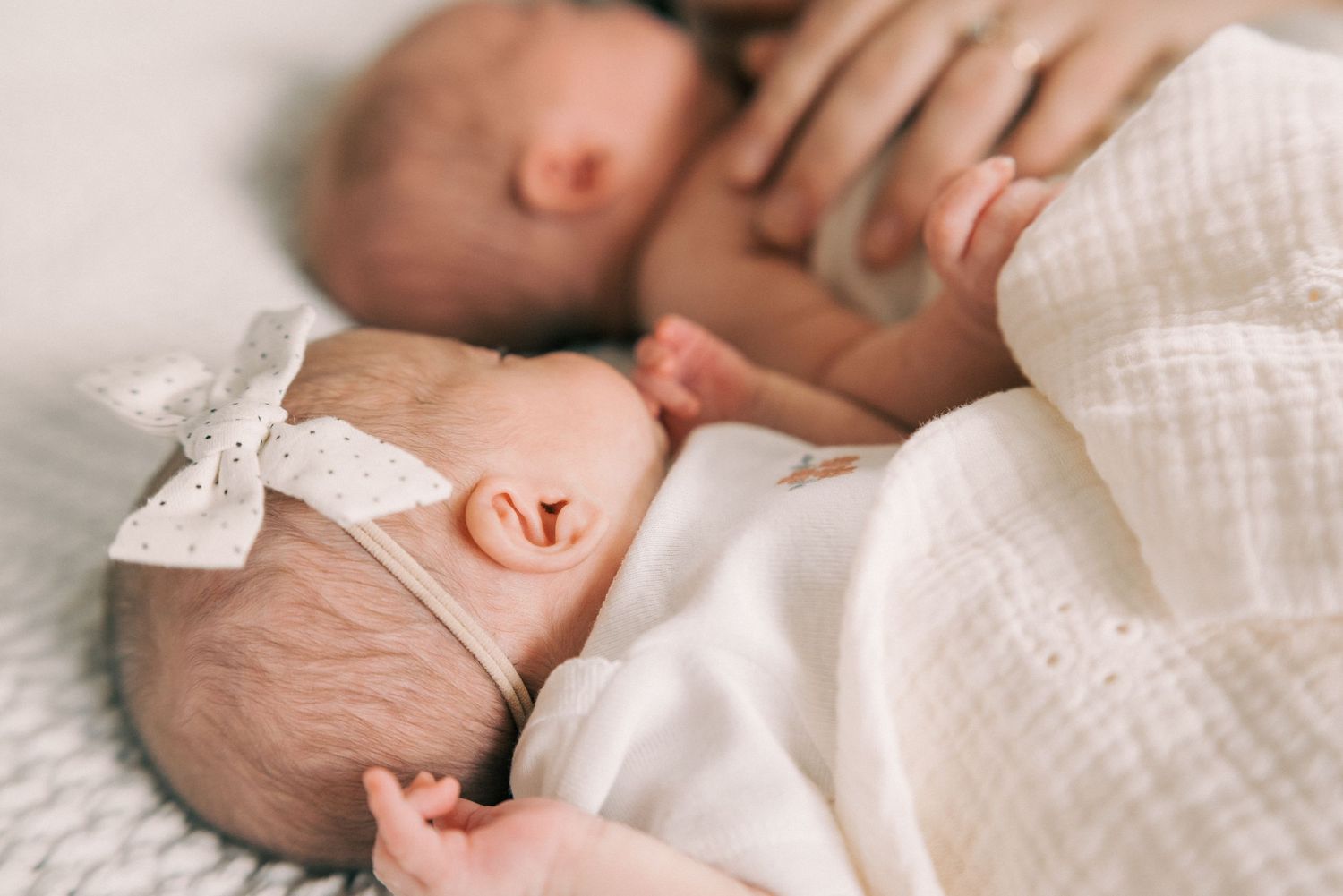 A sleeping newborn swaddled in white with a delicate bow headband.