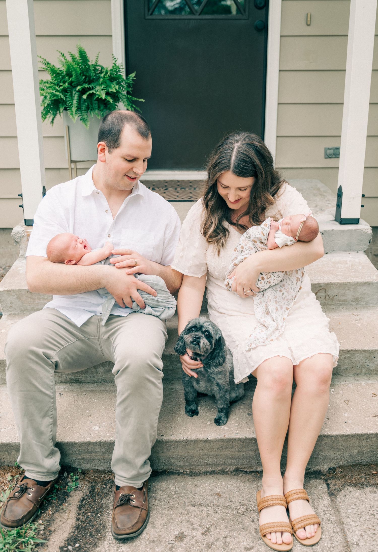 Couple sitting on porch steps with newborn baby and black dog in front of green door.