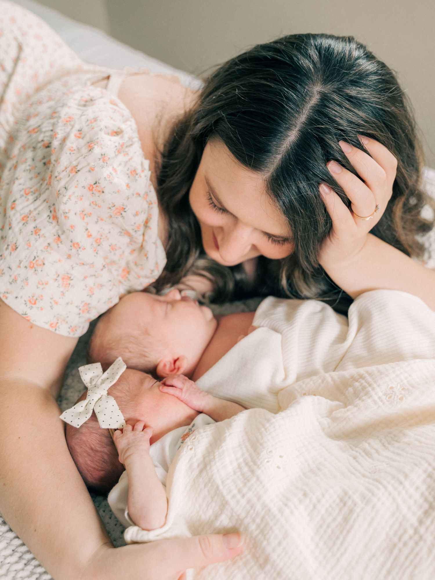 A tender maternal moment with a sleeping newborn wearing a bow.