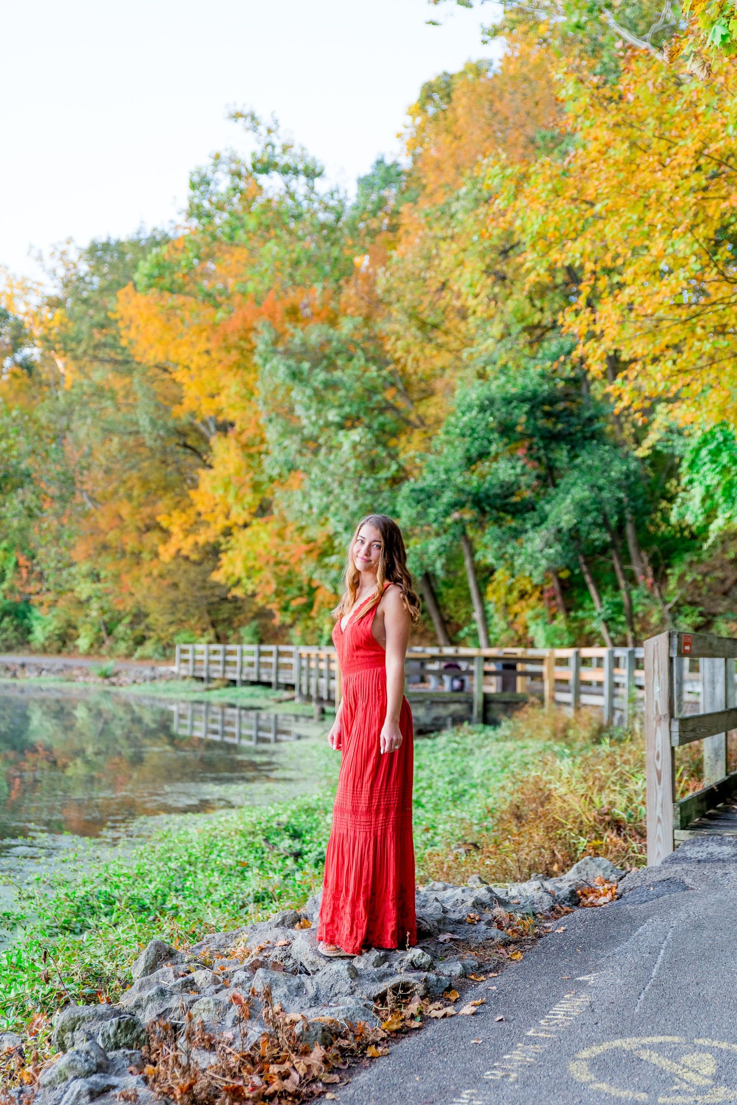 high schooler in orange jumpsuit standing on bridge in Chicago park for senior pictures in the fall