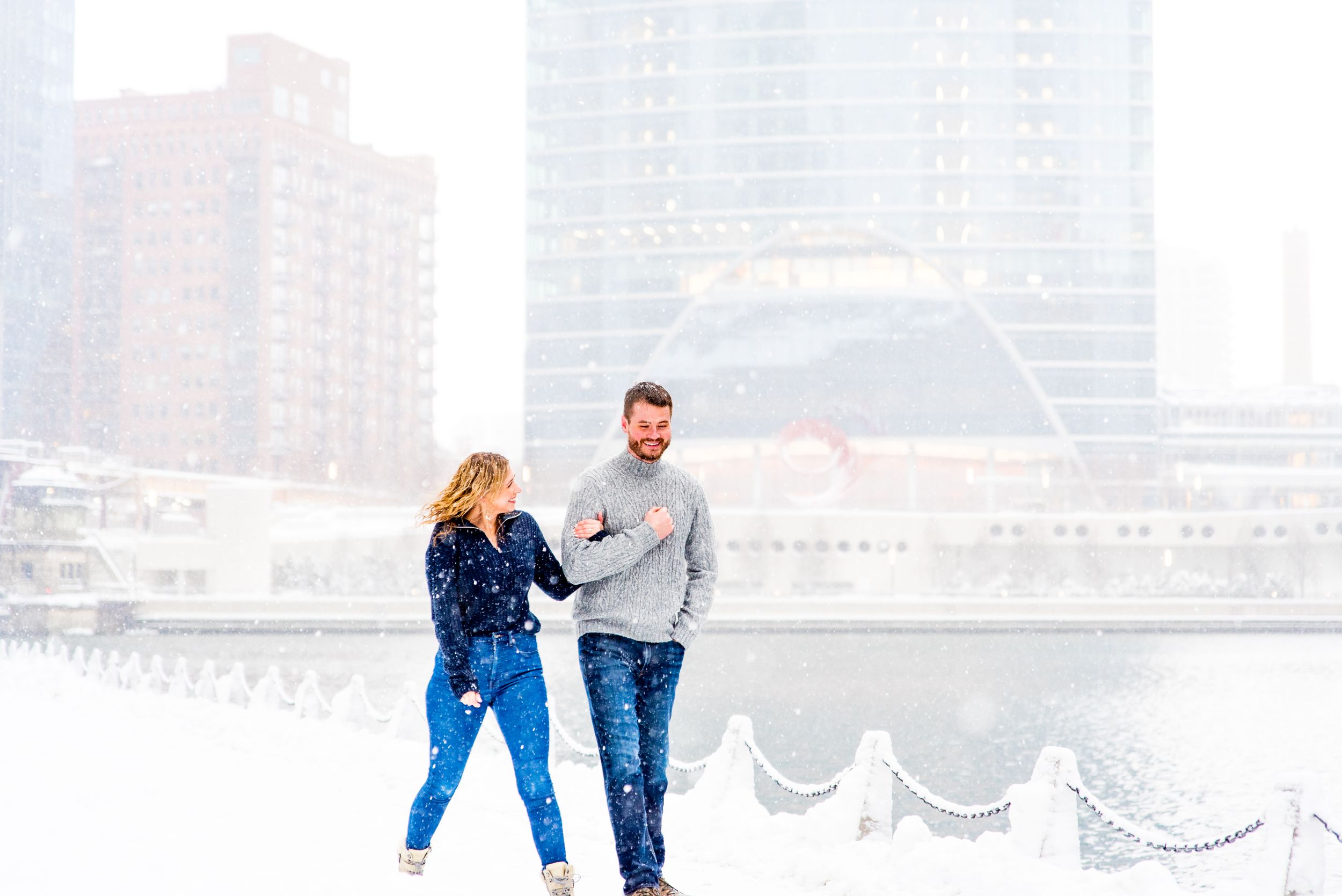 man and woman in navy and grey sweaters smiling in snow at Wolf Point Chicago