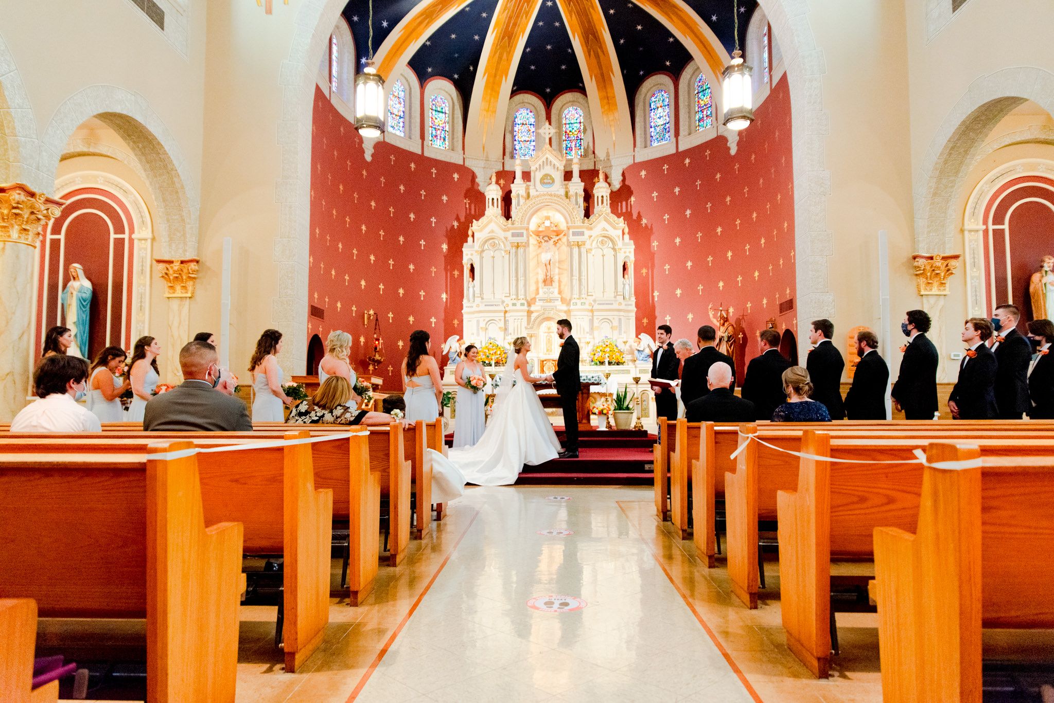 wide image of bride and groom at altar looking at each other and holding hands, showing wedding guests and the church