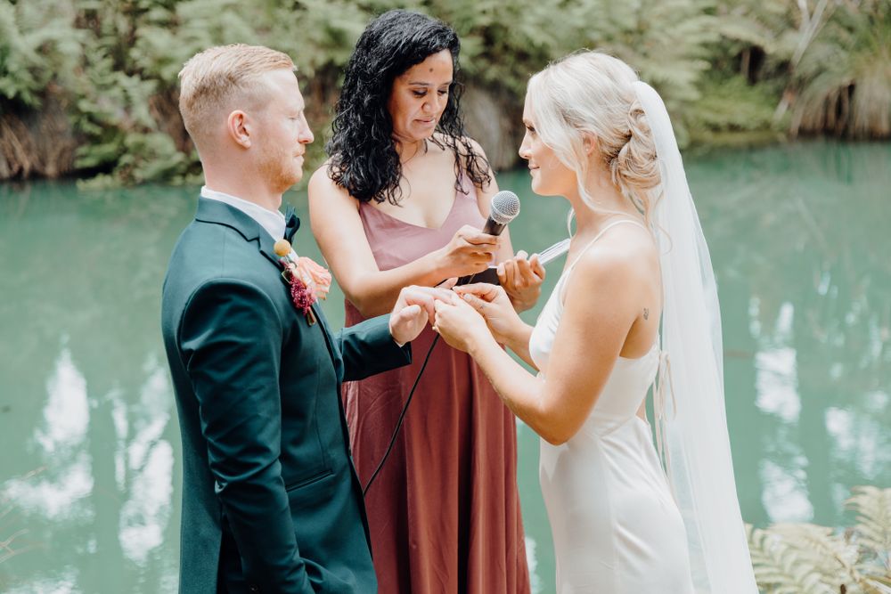 Wedding ceremony exchange of rings beside a serene blue-green lake.