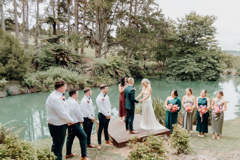 Wedding ceremony takes place beside a tranquil turquoise lake surrounded by lush greenery.
