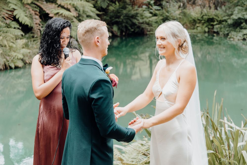 Joyful exchange during wedding ceremony beside serene pond with greenery.