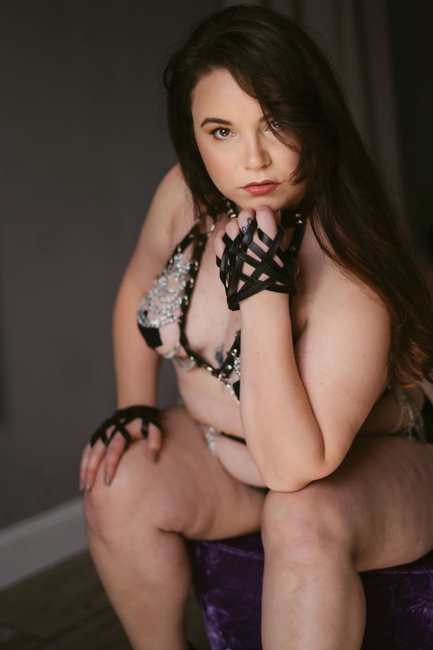 boudoir image of a person in a chain and leather outfit, looking at the camera with confidence