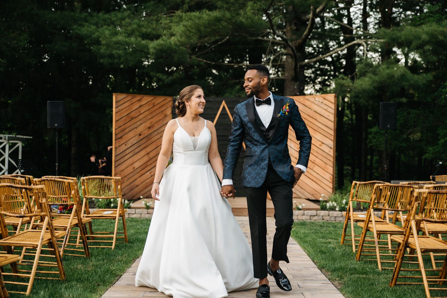 A newlywed couple walks joyfully down the aisle with wooden chairs and decor.