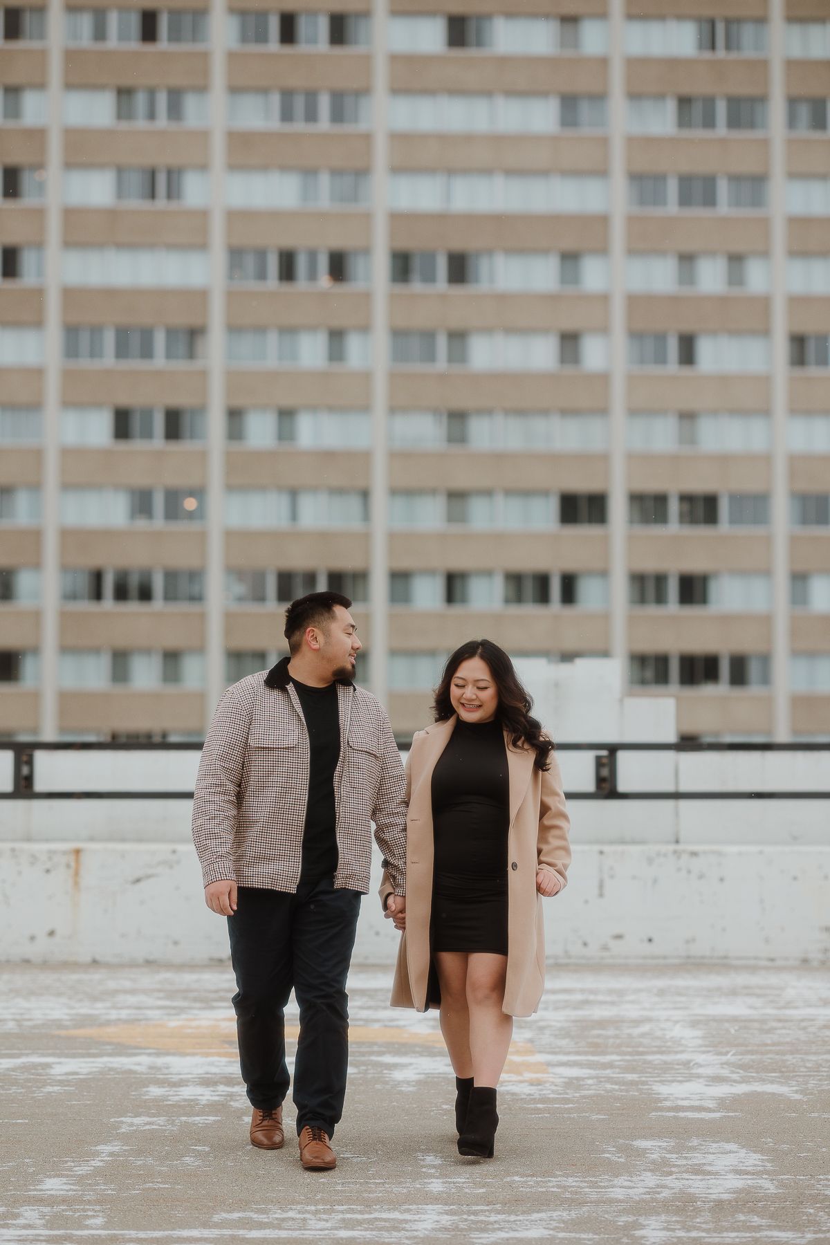 A couple walking together on a rooftop with a high-rise apartment building in the background.