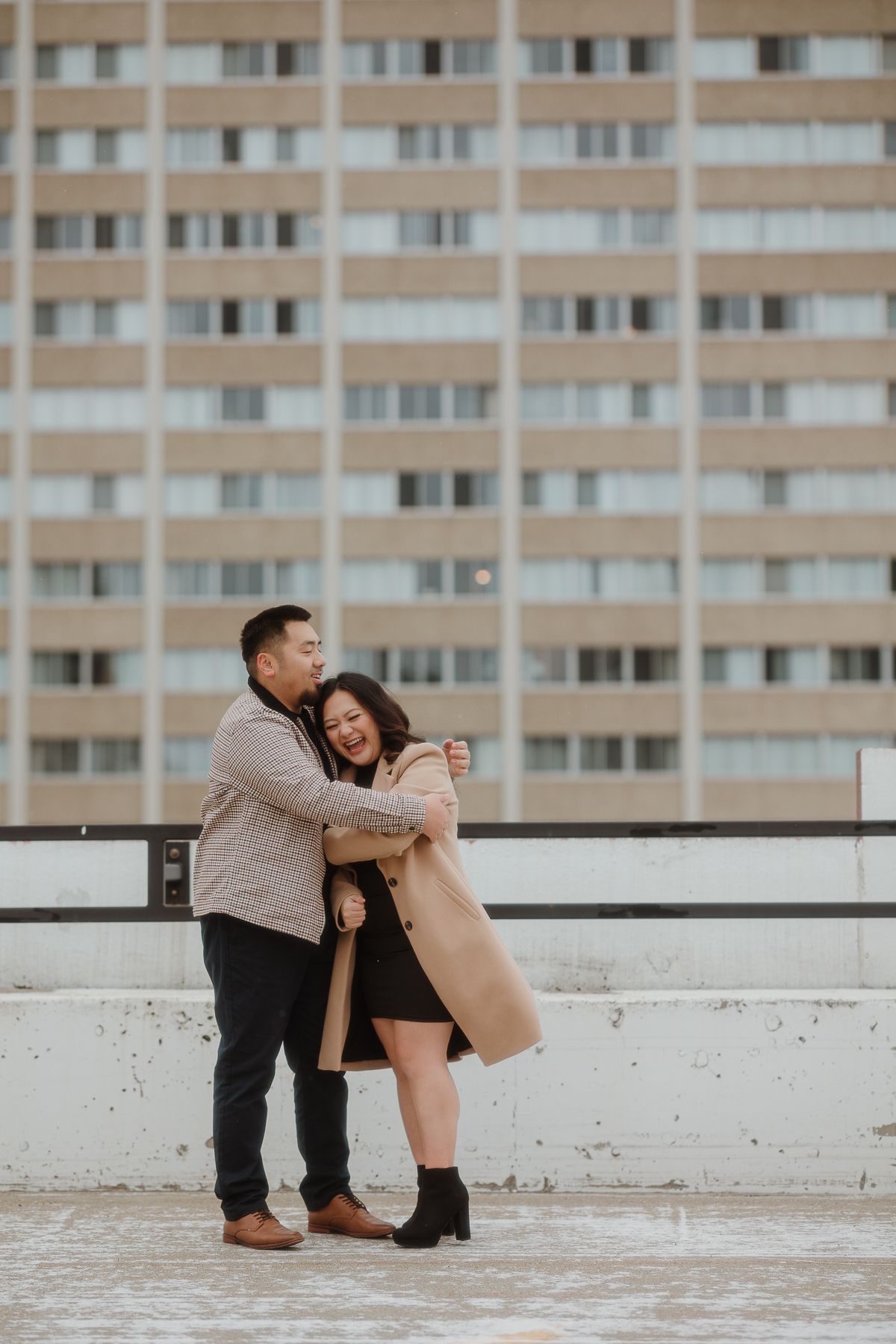 A couple embracing and laughing together on a rooftop with an urban skyline behind them.