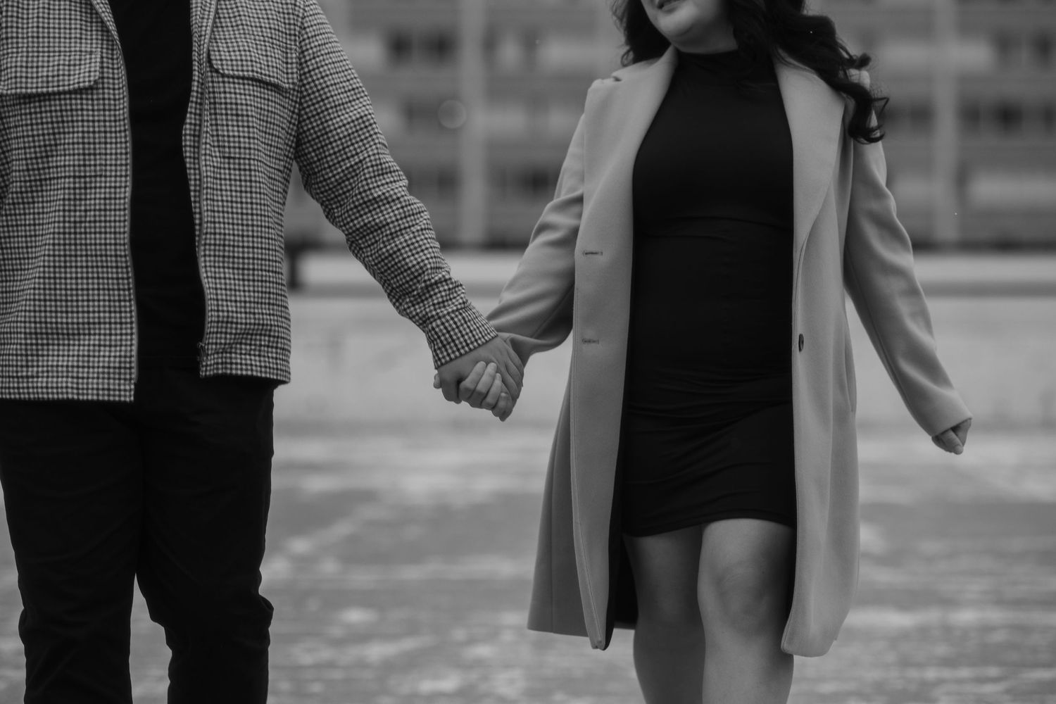A couple holds hands while walking in winter outerwear, shown in black and white.