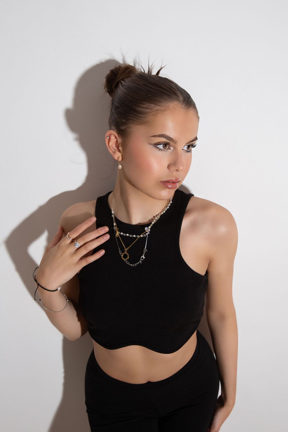 model in black crop top with hair in bun against a white background with large shadow