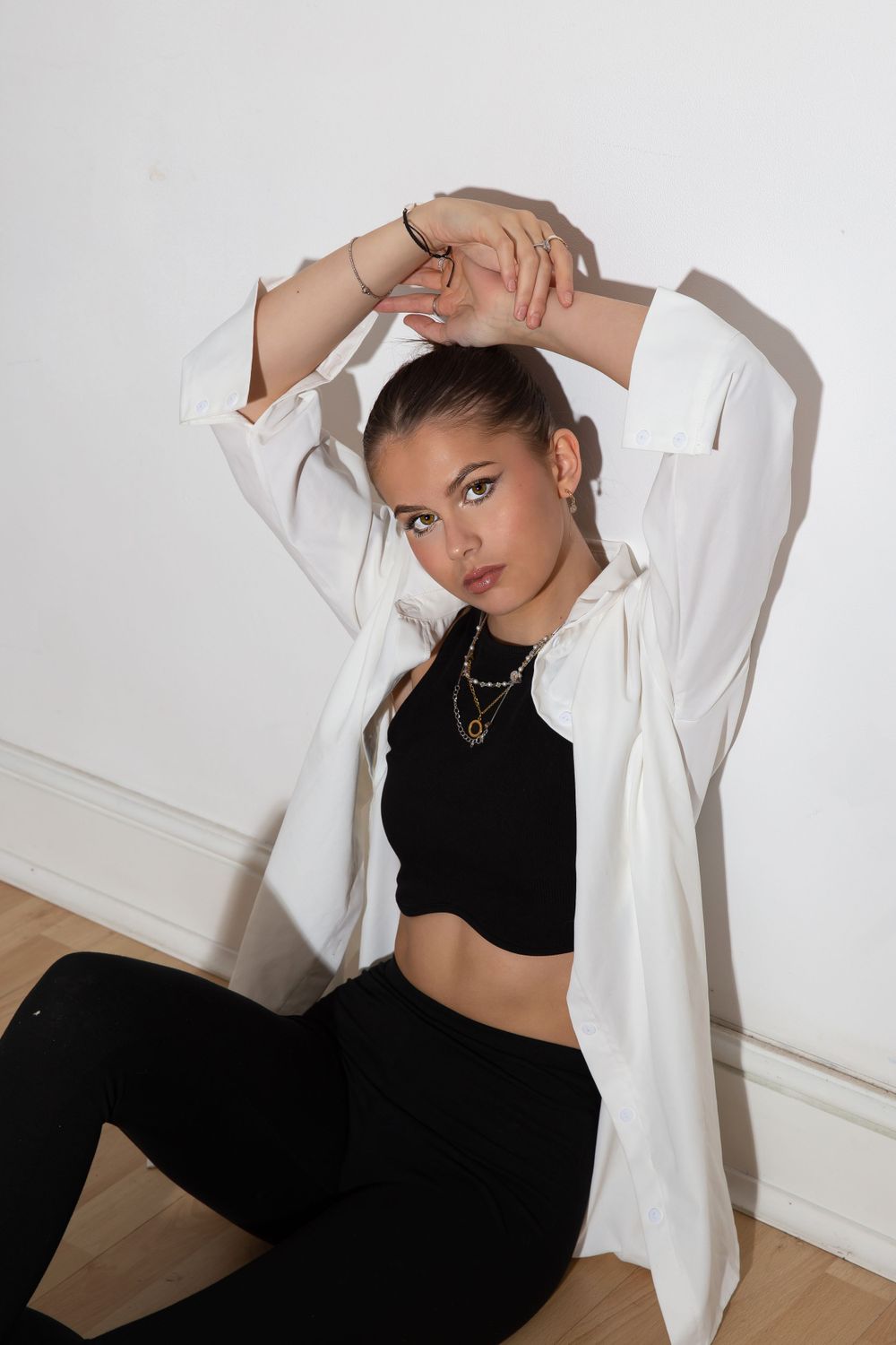 model sat on floor in black crop top and white shirt with arms above head