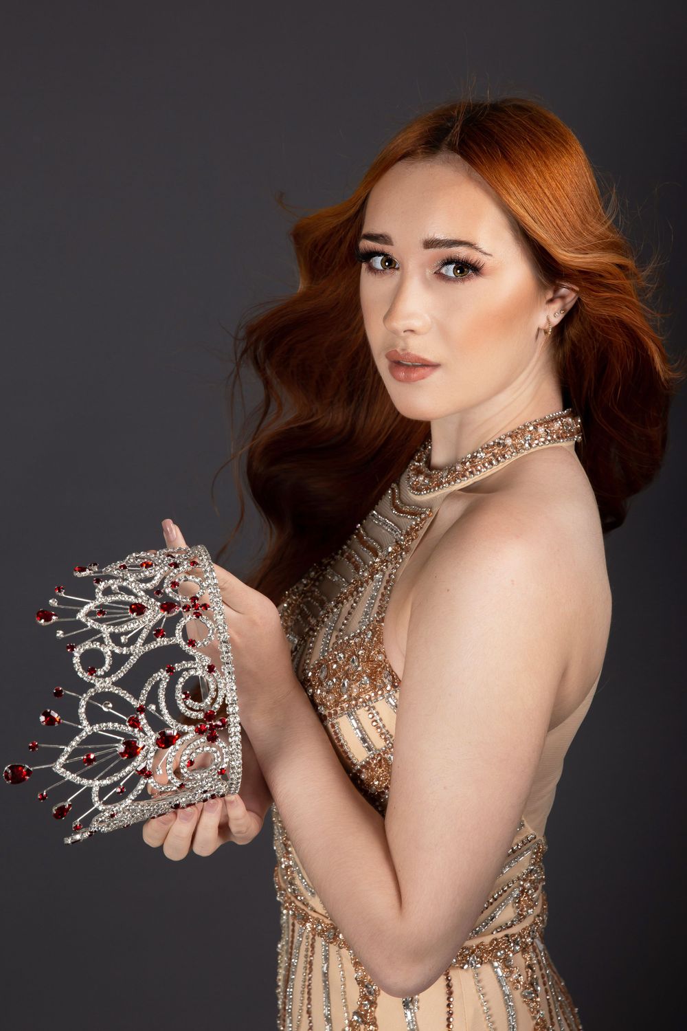 pageant queen holding crown with red hair and gold dress