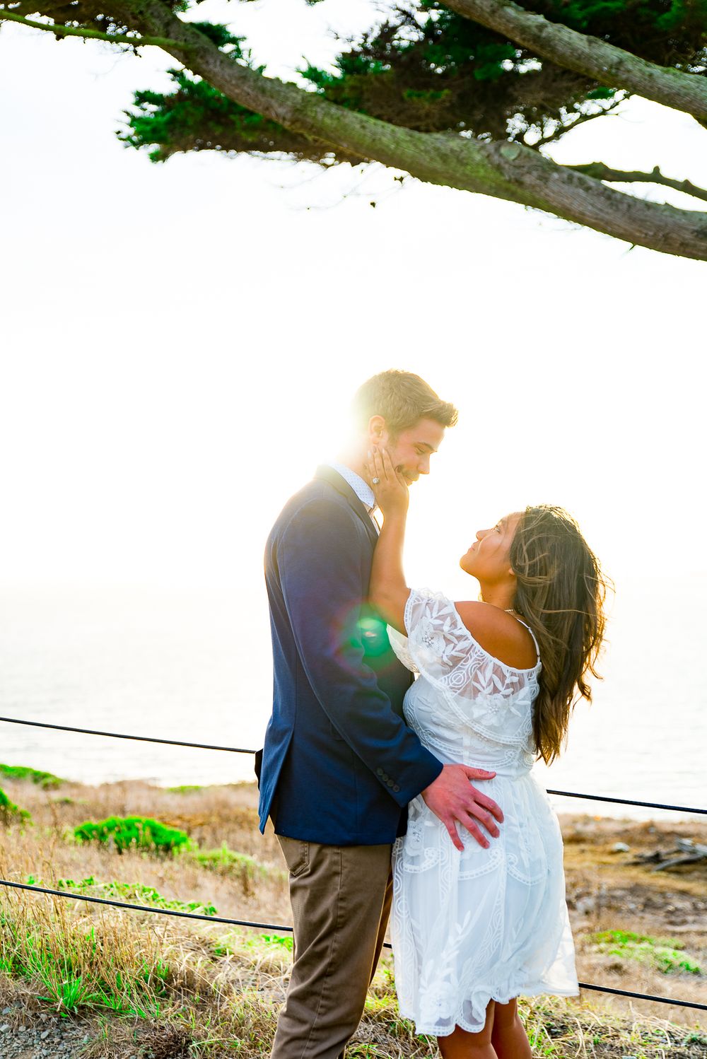 young couple in navy and white standing under tree at sunset in Golden Gate Park engagement photos