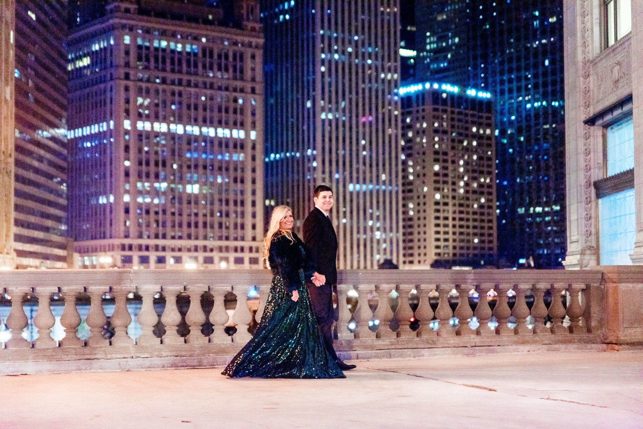 man and woman in suit and green sparkly dress walking at night for Wrigley Building engagement pictures