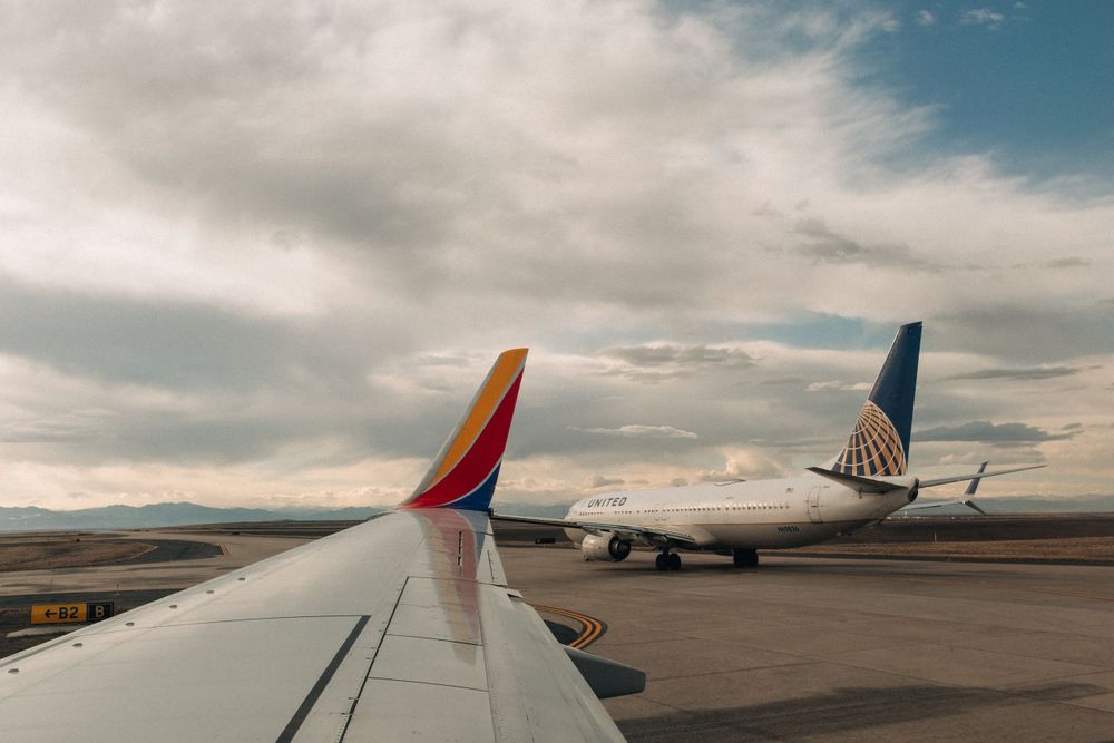 Southwest Airlines wing next to parked United aircraft on airport tarmac under cloudy sky.