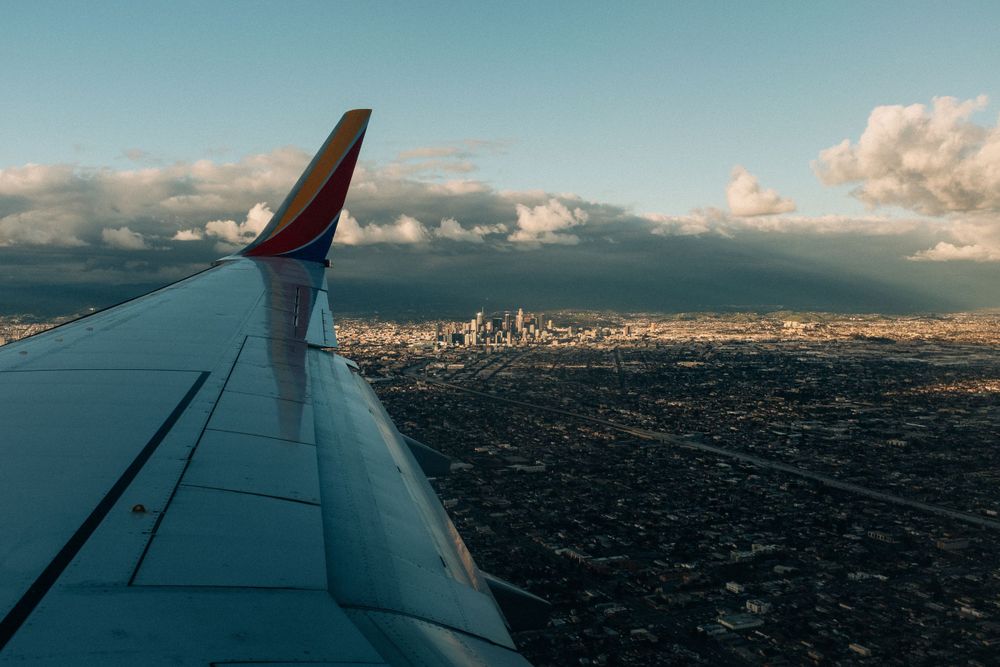 Airplane wing silhouetted against cityscape and mountains during sunset approach.