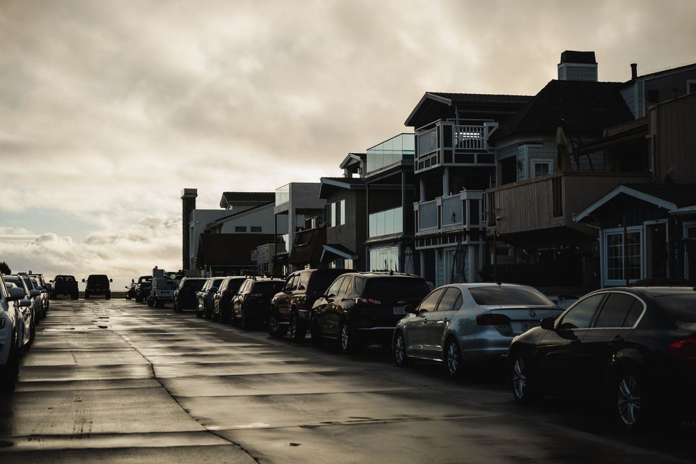 Row of cars parked along beachfront homes on cloudy day.