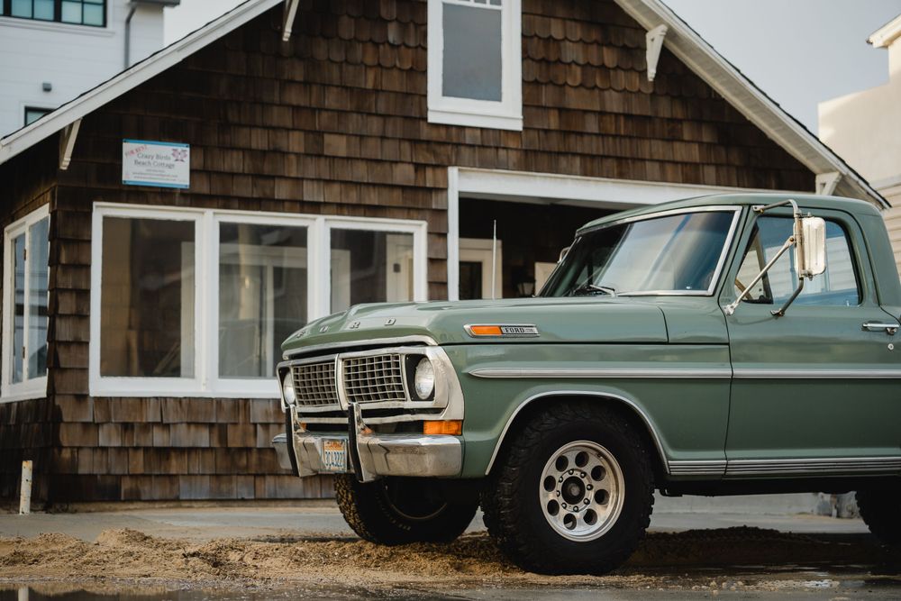 Vintage green Ford pickup truck parked in front of cedar shake house.