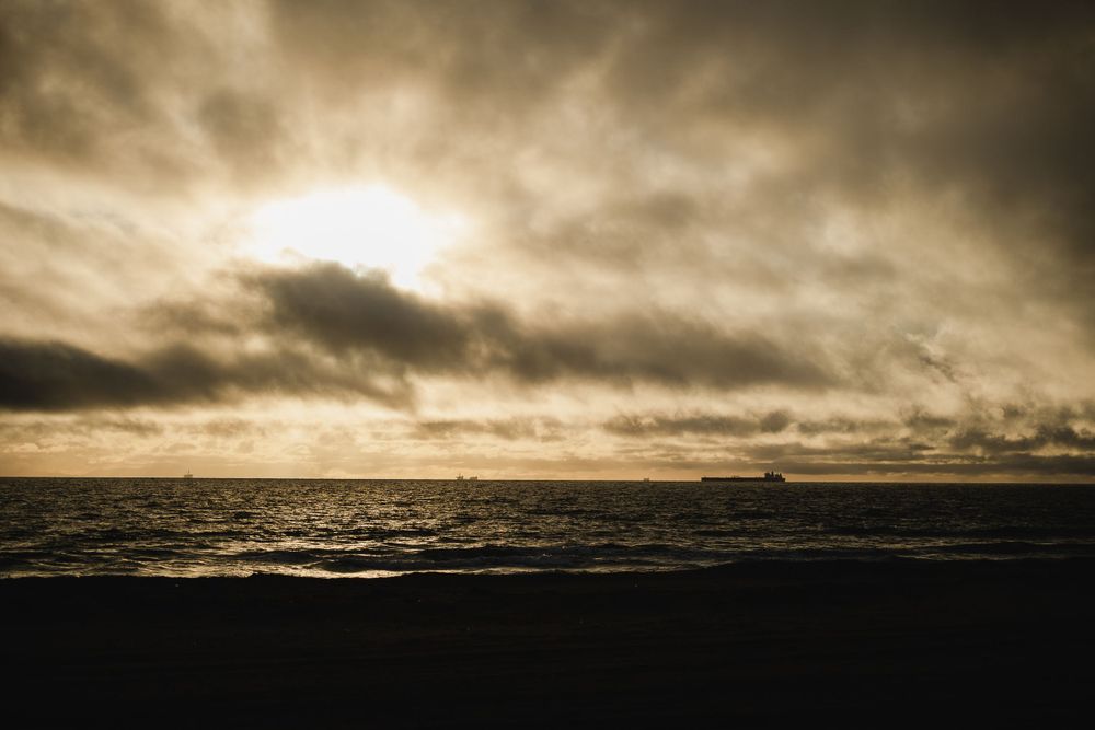 Dramatic sunset over dark ocean waters with moody storm clouds creating a golden atmospheric scene.