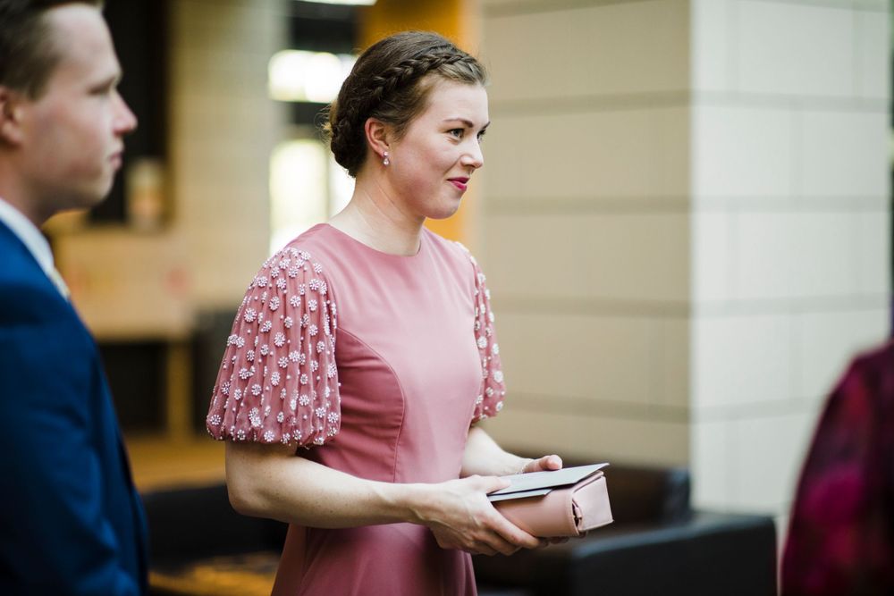 A person in a pink dress with flutter sleeves holds a small package.