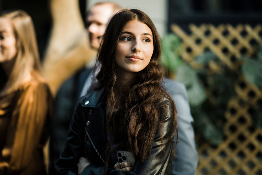 A young woman in a leather jacket smiles while attending an outdoor event.