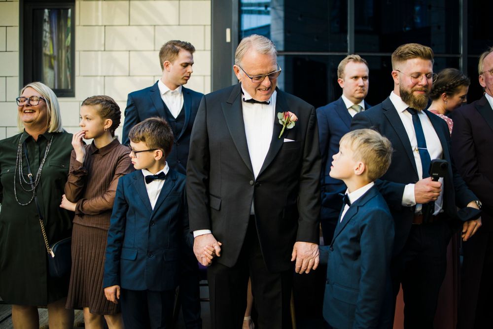 A formal gathering shows multiple generations in suits and formal attire standing together outside a building.
