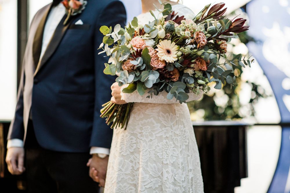 A delicate wedding bouquet with pink and white flowers mixed with eucalyptus held against a white dress.