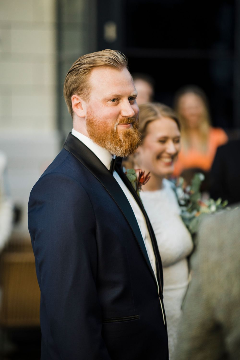 A gentleman in a navy tuxedo with a red beard stands during a formal event.