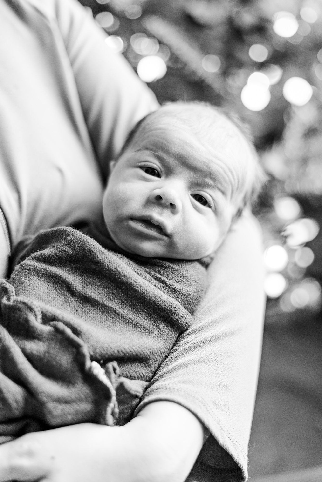 Lifestyle mother holding newborn with Christmas lights behind in black and white in Pittsburgh, Pennsylvania