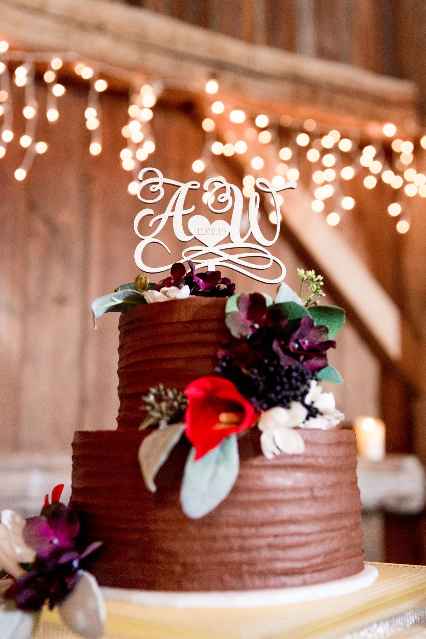 chocolate cake with red and purple flowers and bride and groom initials on top