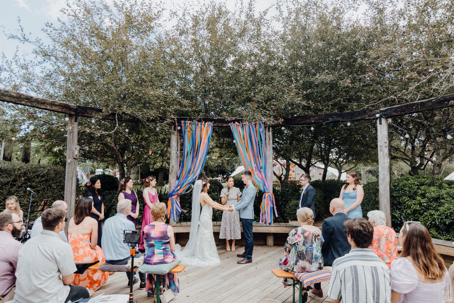 Wide view of intimate outdoor wedding ceremony with hanging streamers and seated guests.