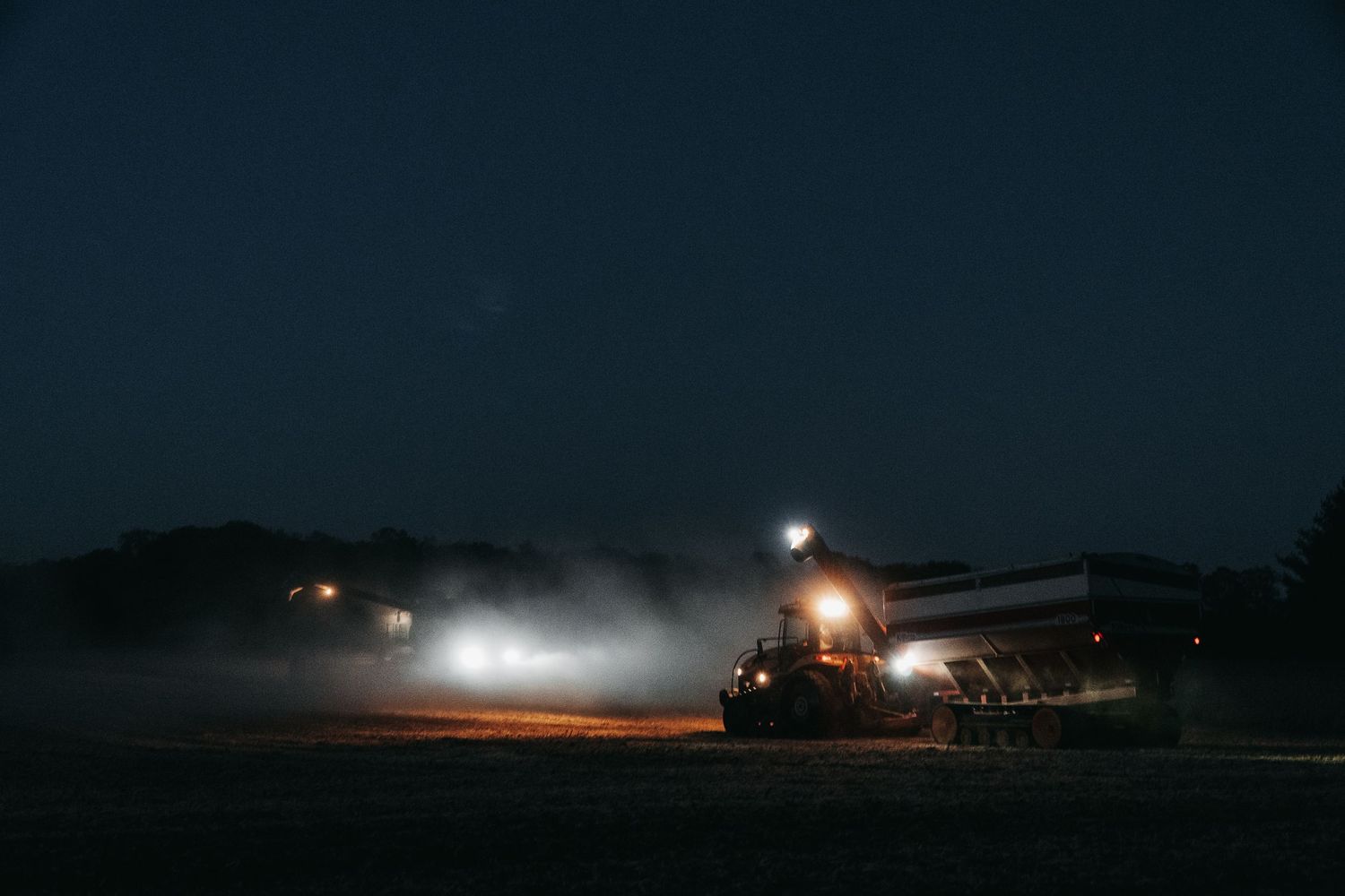 Agricultural harvester operating in misty field at night with glowing lights.