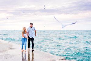 young engaged couple holding hands and laughing while they walk along North Avenue Beach pier