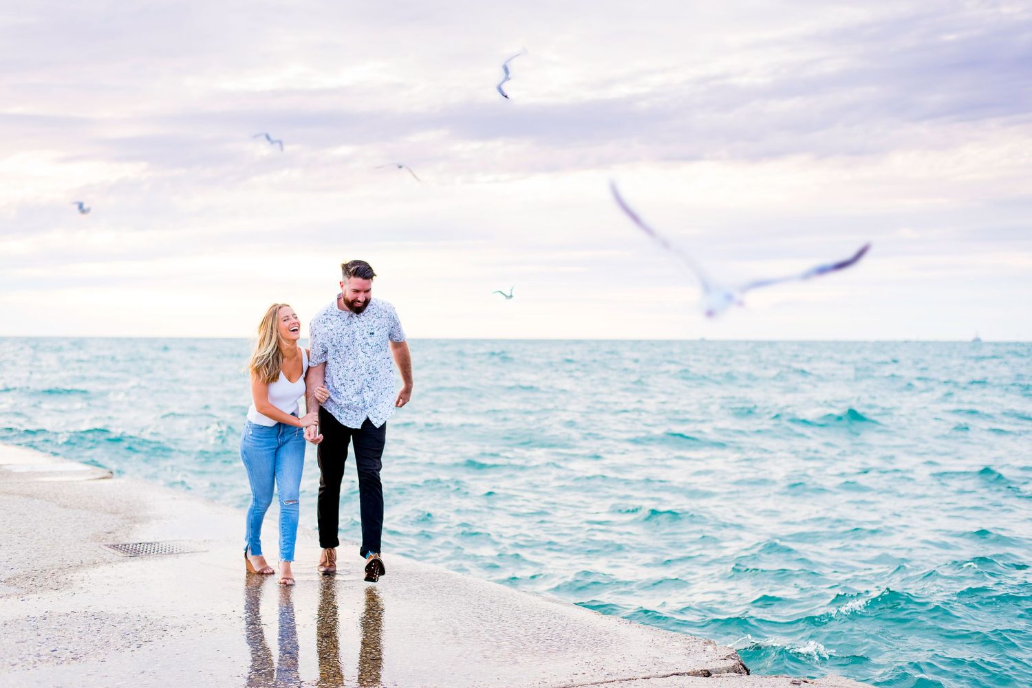 young engaged couple holding hands and laughing while they walk along North Avenue Beach pier